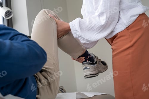 Preview: Physical therapist in white blouse assisting a patient with a knee exercise in a clinical setting.