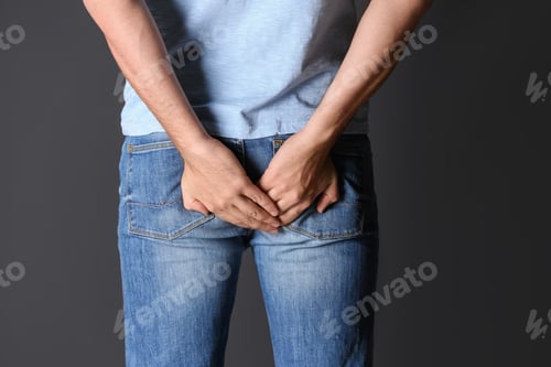 Preview: Man suffering from hemorrhoid on black background, closeup