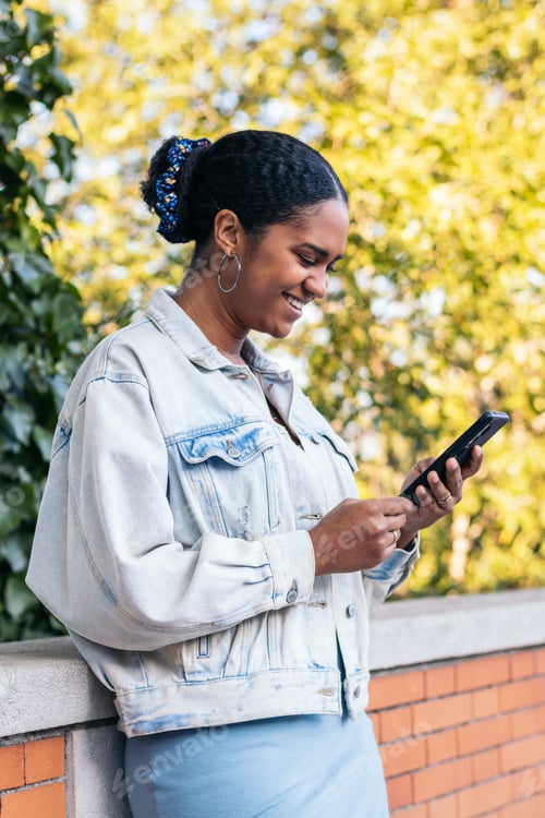 Preview: African-American girl using a smartphone in the park on a summer day.