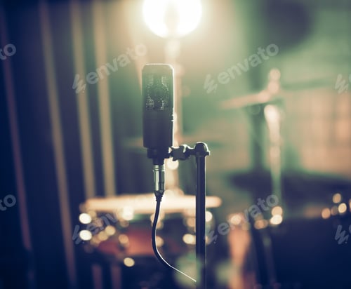 Preview: Microphone in recording Studio or concert hall close-up, with drum set on background out of focus.