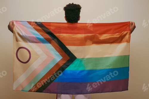 Preview: back view of african american man holding rainbow lgbt flag on yellow background, pride month