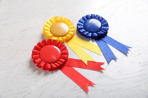 Preview: Different award ribbons on white wooden table, closeup. Space for text