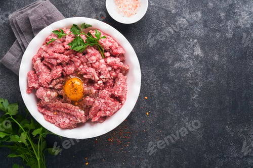 Preview: Raw minced meat. Ground meat beef, pork or lamb spices, herbs and eggs on white plate on black old c
