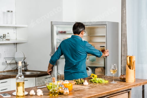 Preview: rear view of mature man looking into fridge in kitchen