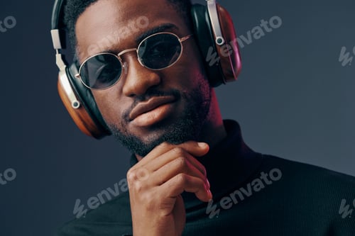 Preview: Stylish man with headphones in sunglasses, exuding confidence against a dark background, showcasing