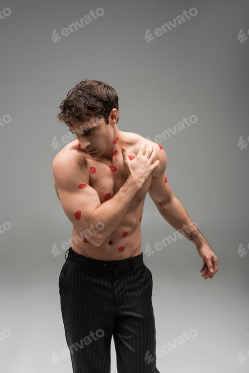 Preview: athletic man in black trousers posing with red lip prints on muscular torso on grey background