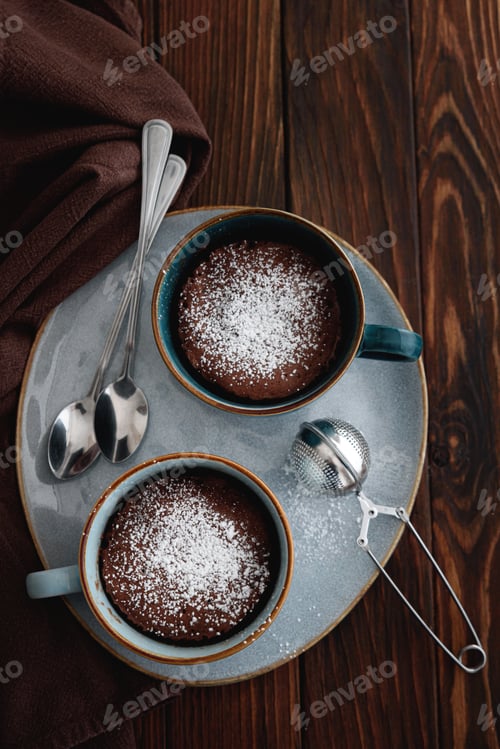 Preview: Two chocolate mug cake under sugar icing on dark wooden table
