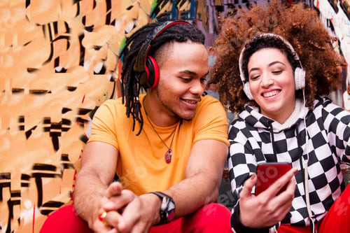 Preview: Two friends wearing headphones, listening to music, holding smartphone
