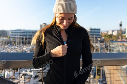 Preview: Sportswoman zipping up her jacket before training in a marina