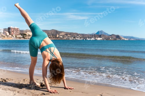 Preview: Woman practicing three-legged downward-facing dog pose on the beach