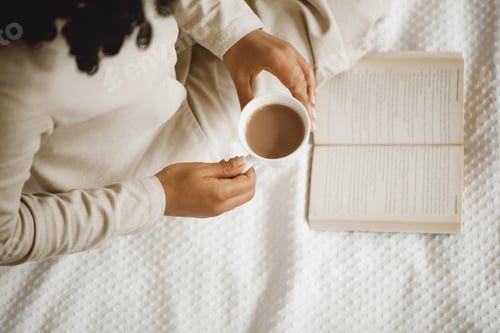 Preview: Woman’s hands holding cup of coffee over the open book.