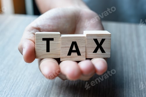 Preview: Business woman hand holding wooden cube with TAX text on table background.