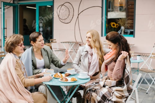 Preview: Company of senior woman having breakfast on a terrace of a street cafe after shopping