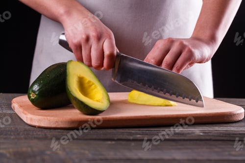 Preview: A young woman in an gray apron cuts an avocado on a wooden cutting board