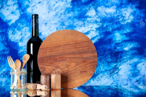 Preview: Top view of round cutting board and glass bottle wooden spoons and fork salt pepper pots on blue and