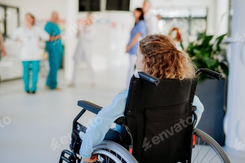 Preview: Rear view of little girl with teddy bear sitting on wheelchair.