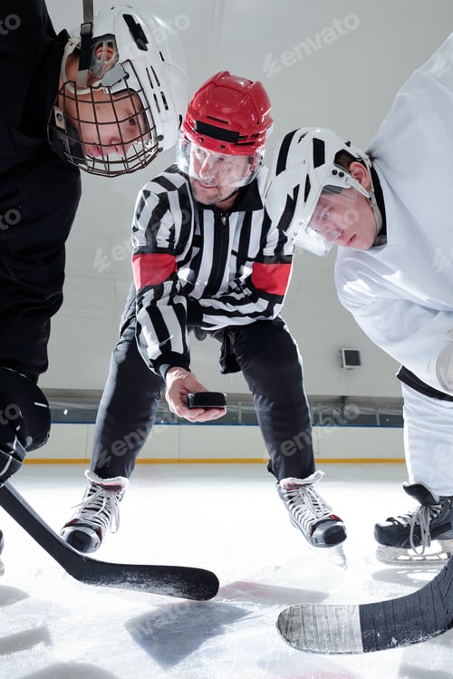 Preview: Hockey referee holding puck over ice rink while rivals with sticks looking at it