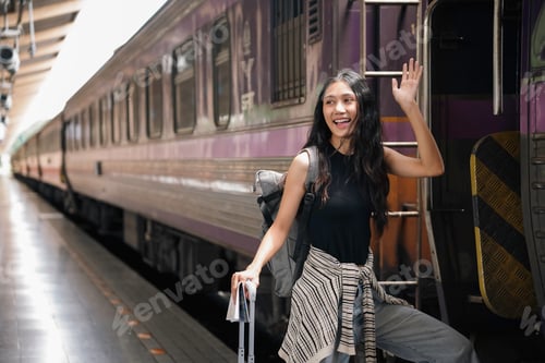 Preview: Happy young backpacker woman holding passport and boarding a train waving goodbye