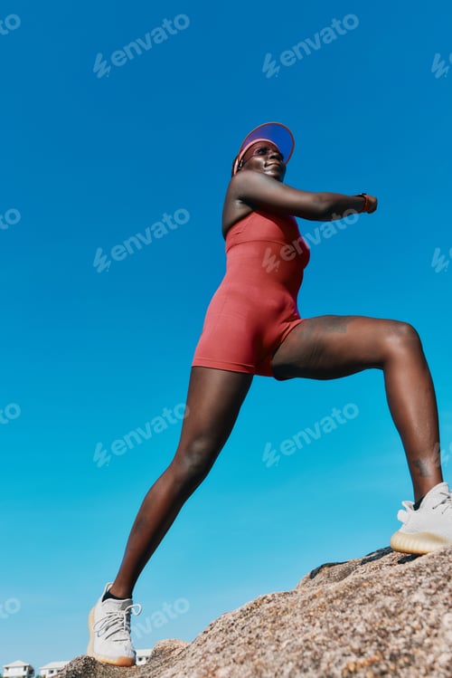 Preview: A confident woman in a red outfit stands on a rock against a clear blue sky, showcasing strength and