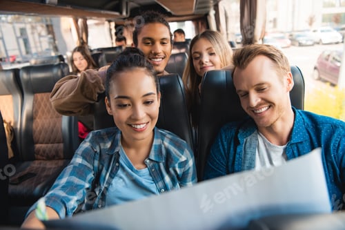 Preview: cheerful multiethnic tourists looking at map during trip on travel bus