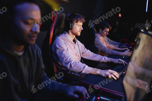 Preview: Gamer in headphones playing video game on computer near multiethnic team in cyber club