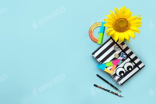 Preview: School accessories striped black and white notebook, pen, pencile and sunflower on blue background