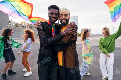 Preview: Two men at pride parade celebrating the LGBTQIA month hugging and looking at camera cheerfully.