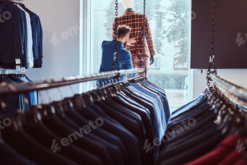 Preview: Stylish bearded seller care about suit on a mannequin in a menswear store.