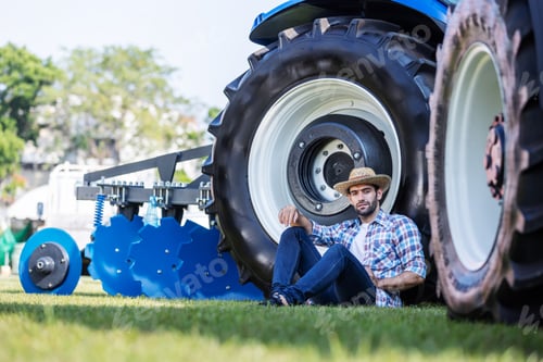 Preview: Farmer sits relaxed beside a large blue tractor