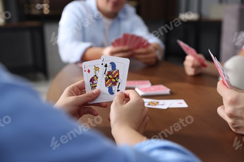 Preview: Friends playing cards at wooden table indoors, selective focus