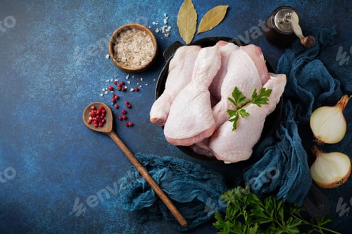 Preview: Raw chicken legs on a cast iron pot with spices and herbs on a dark concrete or stone background pre