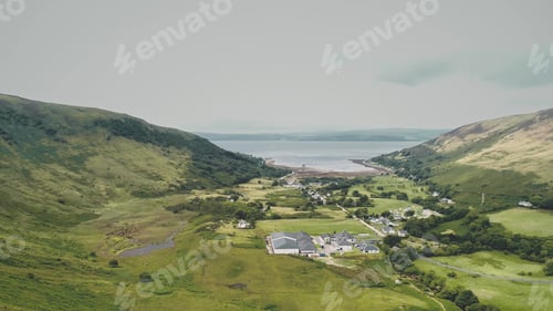 Preview: Scotland village at green mountain valley aerial. Scottish hillside town with sea lake, castle ruins