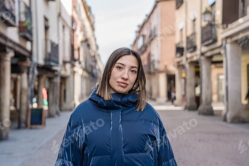 Preview: Young woman wearing blue padded jacket walking in city center
