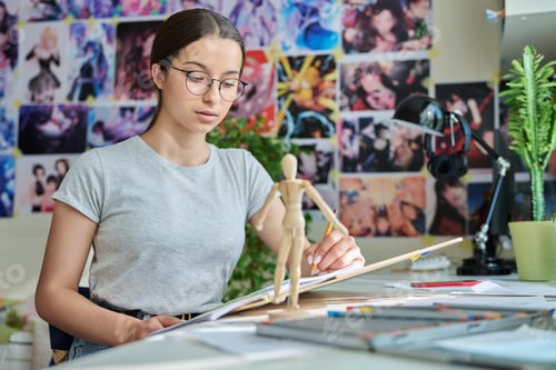 Preview: Teenage creative girl artist drawing with a pencil, sitting at the table at home