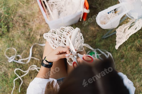 Preview: Woman knits bag using macrame technique outdoors near tents. Outdoor hobbies.