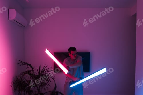Preview: Mid adult man funny with led neon laser at home, samurai or Jedi