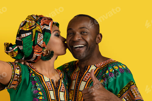 Preview: Cheerful black couple in african costumes taking selfie on yellow