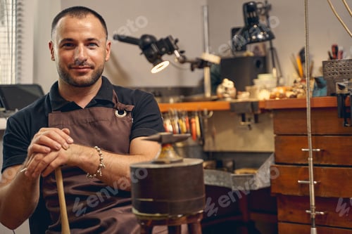 Preview: Smiling jeweler sitting in front of the anvil