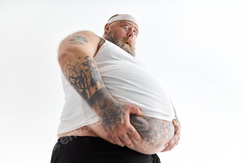 Preview: fat man with big belly and tattoes in sports wear is holding his stomach with shocked emotion