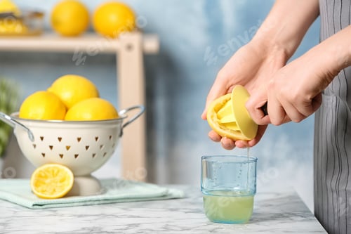 Preview: Woman squeezing lemon juice with reamer into glass on table