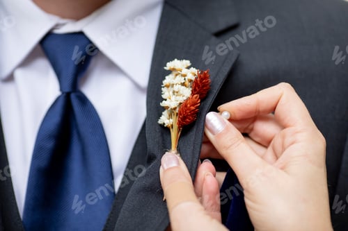 Preview: Detail shot of hands pinning on a boutonnniere on a grooms suit