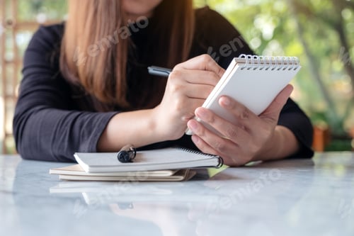 Preview: A business woman holding and writing on notebook in cafe with green nature background