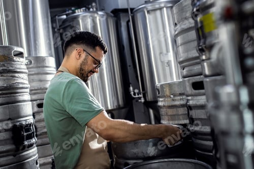 Preview: Man working in craft brewery examining production of the beer.