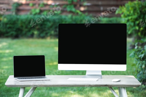 Preview: selective focus of laptop and computer with blank screens at table outdoors