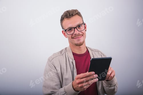 Preview: A smiling young man uses his tablet, studio shot with white background
