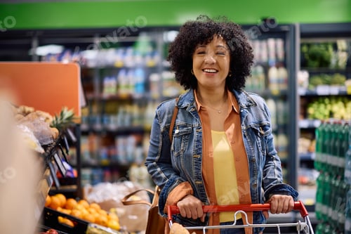 Preview: Happy mature woman buying groceries in a supermarket and looking at camera.