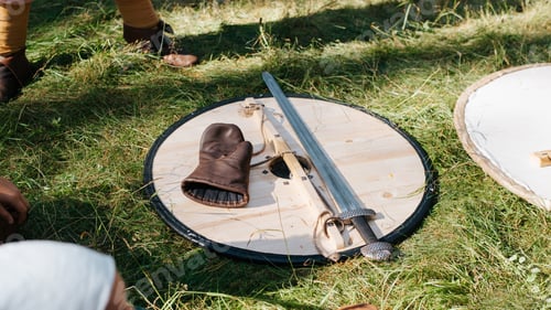 Preview: Armament of a viking medieval warrior sword, wooden shield and glove lying on the grass outdoors