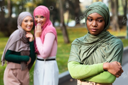 Preview: Arabic Ladies Whispering Behind Back Of Black Muslim Woman Outdoors