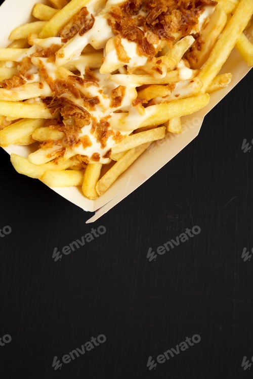 Preview: French fries with cheese sauce and fried onion in a paper box on a black background, top view.