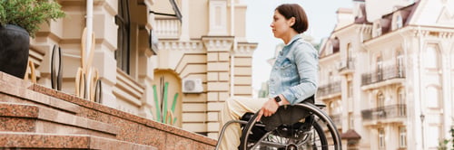 Preview: Brunette woman sitting in wheelchair by stairs on city street